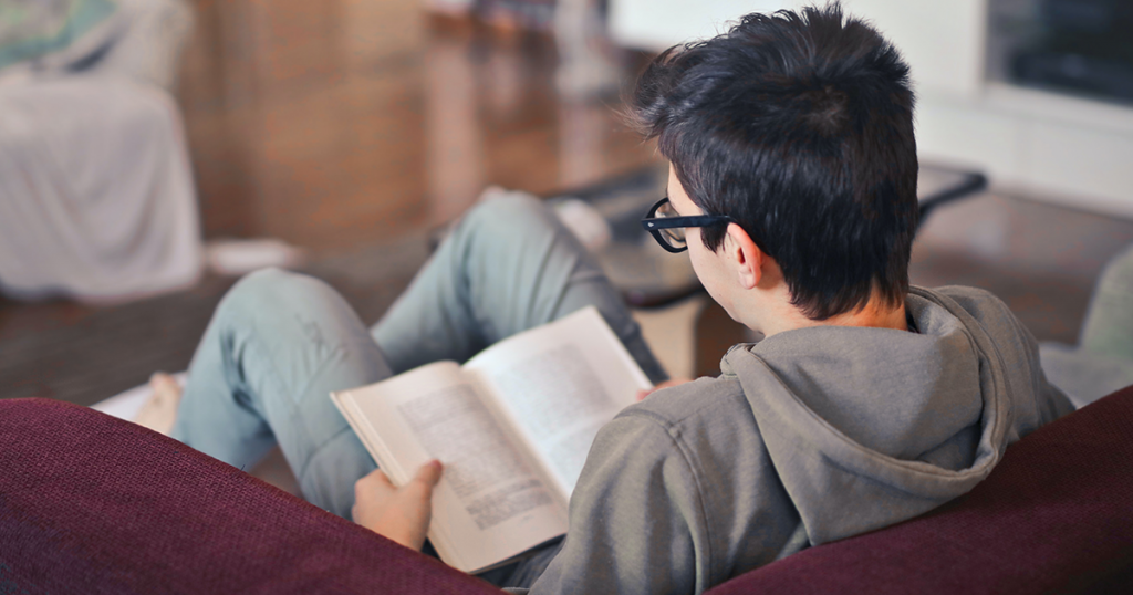 Teen boy reading on couch in library