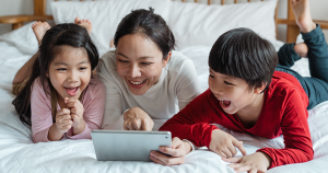 An adult and two children look at a tablet together and laugh