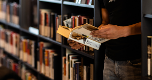A person's hands holding a book in front of library bookshelves