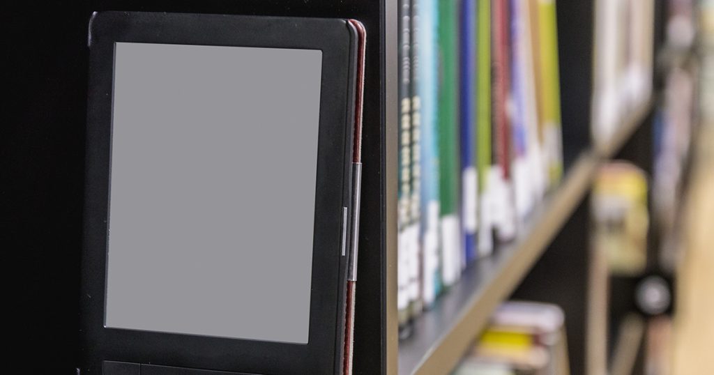 E-book reader sitting on shelf with library books