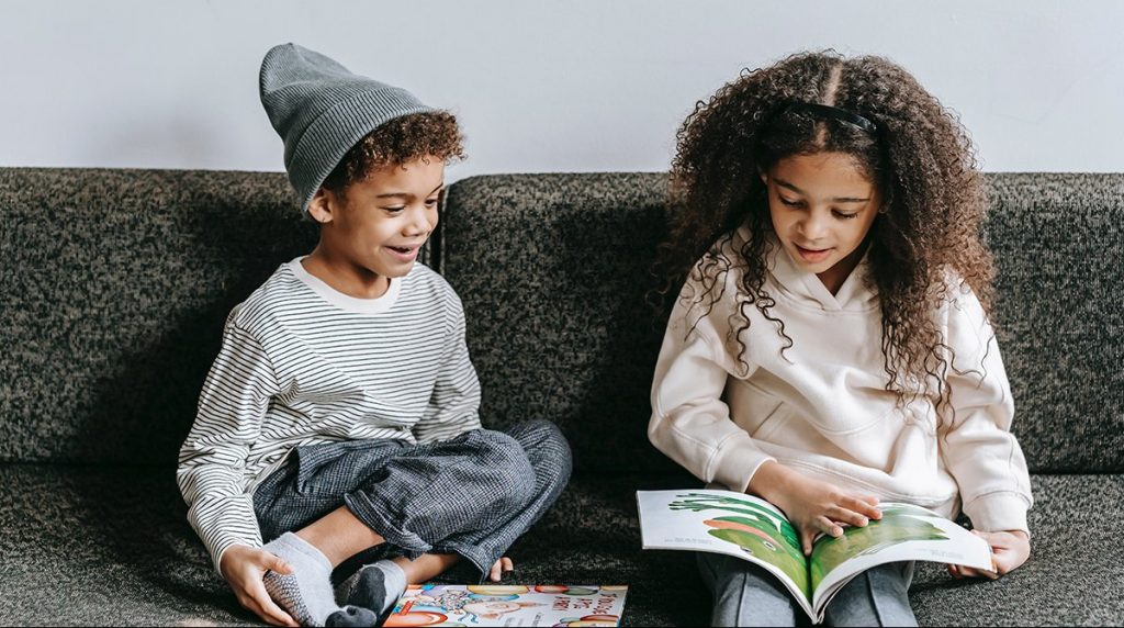 Two black children enjoying reading together on a couch
