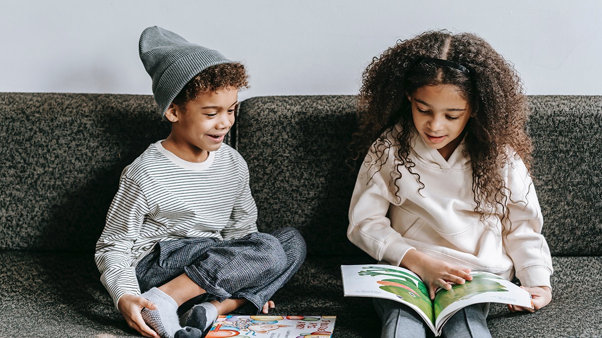 Two black children enjoying reading together on a couch