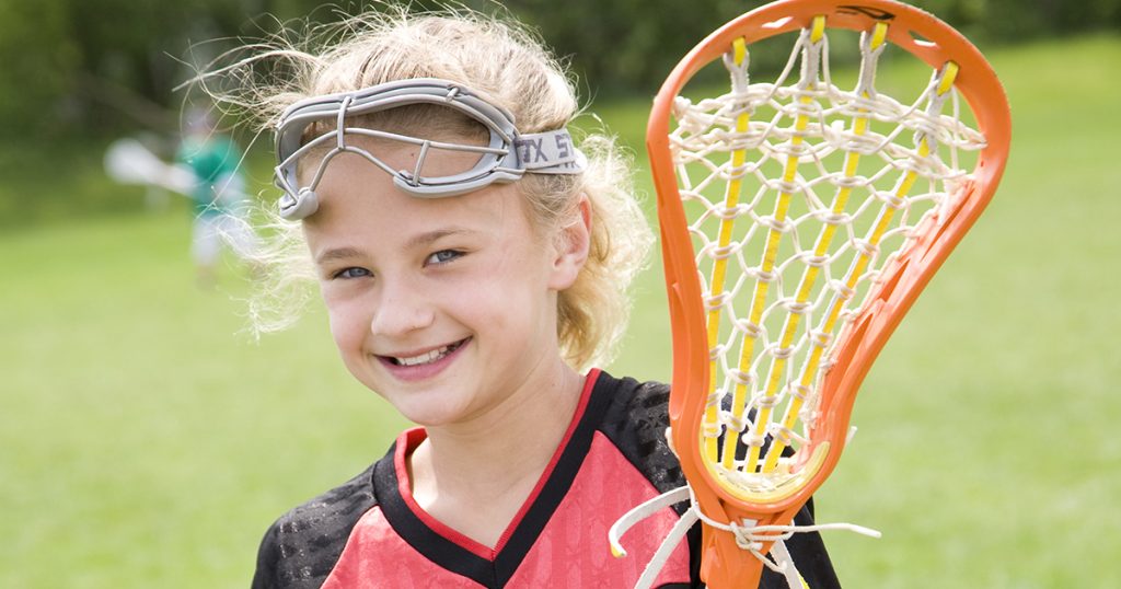Smiling girl holding a lacrosse sprts gear