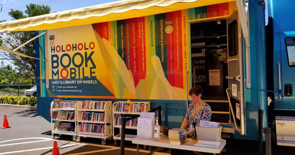 A person sits at a table in front of a library bookmobile