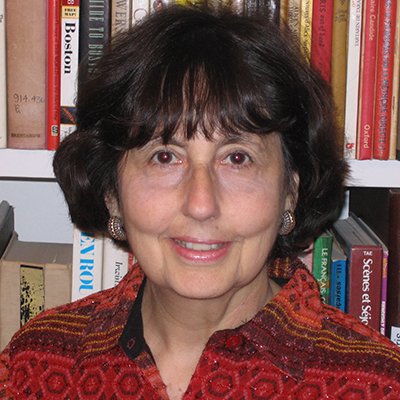 Photo of woman with dark hair waring a red patterned shirt and smiling in front of library shelves