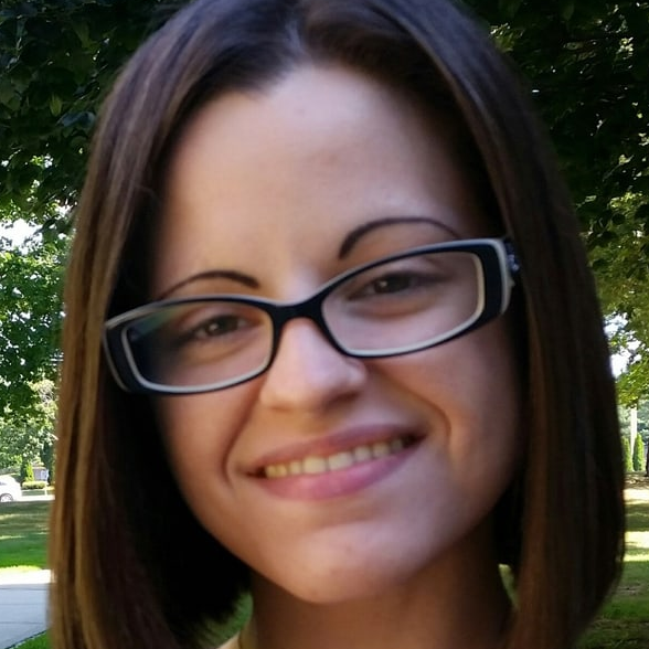 Photo of a woman with dark hair and glasses outside smiling