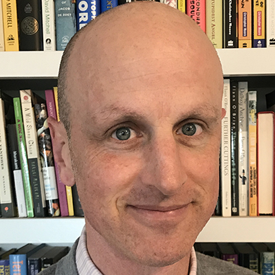 Photo of bald man in front of library shelves
