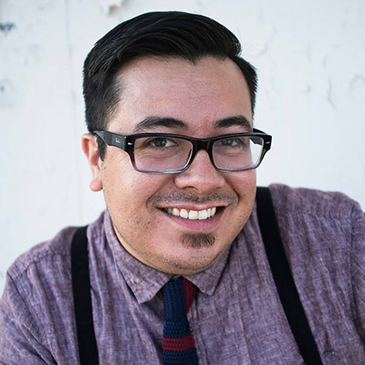 Photo of a man with short dark hair and glasses wearing suspenders and a tie and smiling