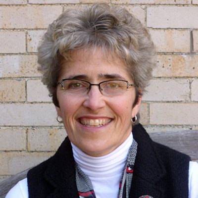 Photo of a woman with gray hair and glasses wearing a white shirt and vest and smiling
