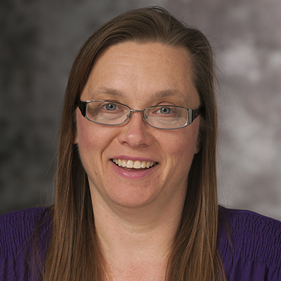 Photo of a woman with long hair and glasses and a purple shirt smiling