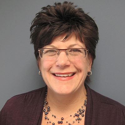 Photo of woman with short dark hair wearing a maroon cardigan and necklace and smiling
