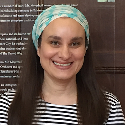 Photo of a woman with long hair and a head scarf and a strip shirt smiling