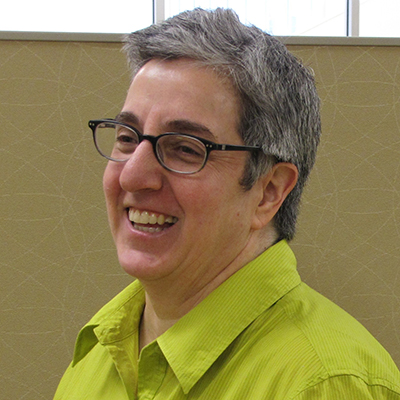Photo of woman with short gray hair and glasses wearing a yellow-green shirt smiling away from the camera
