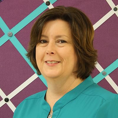 Photo of a woman with brown hair and a turquoise shirt in front of a patterned background