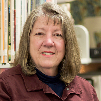 Photo of a woman in a collared shirt in front of library shelves