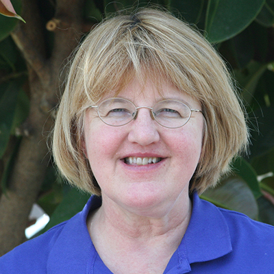 Photo of woman with blonde hair and glasses wearing a blue shirt and smiling