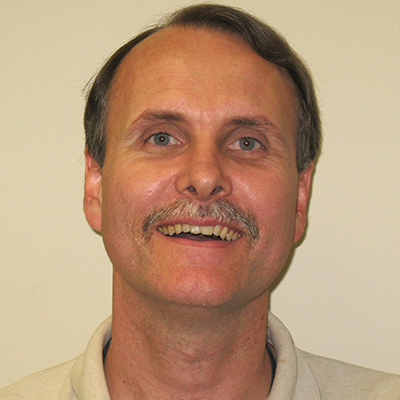 Photo of a man with gray hair and a mustache smiling