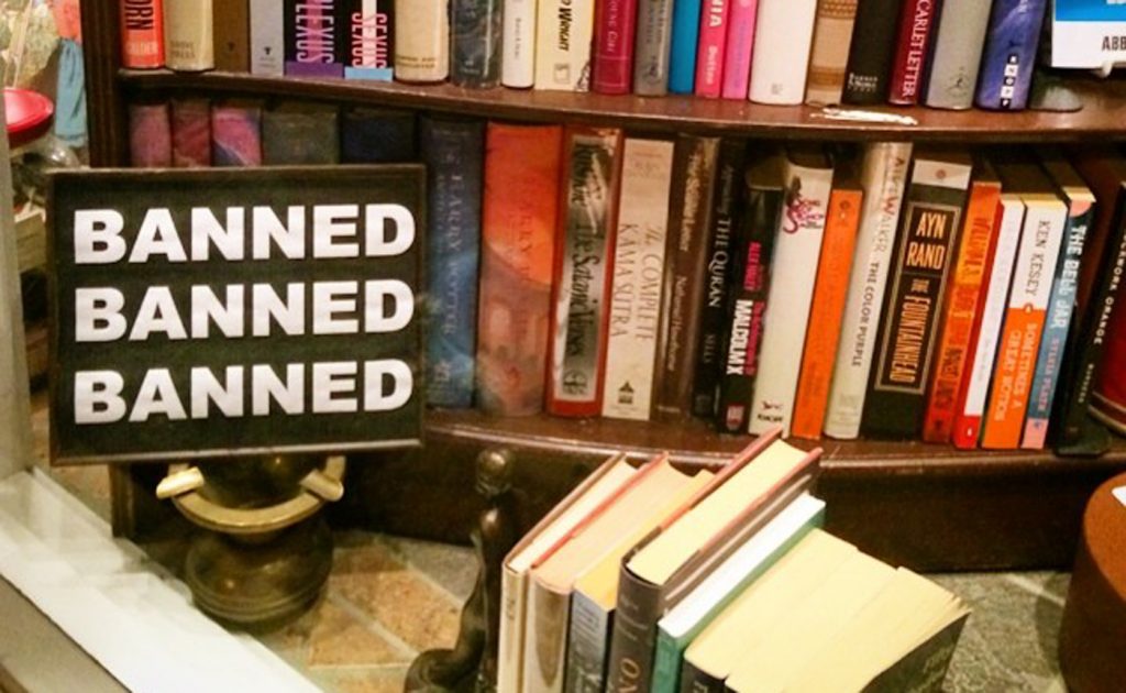 A sign reading "Banned, Banned, Banned" sits in front of library shelves.
