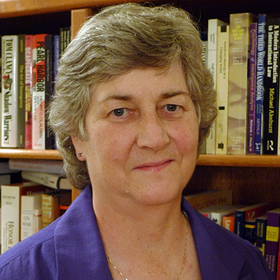 Photo of a woman with gray hair wearing a purple jacket in front of library shelves