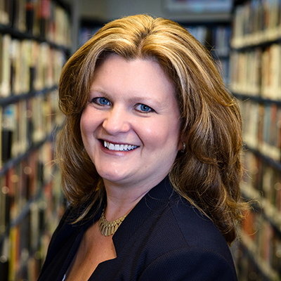 Photo of woman with blonde streaked hair between library stacks smiling