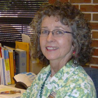 Photo of a woman with curly hair and glasses wearing a patterned shirt and smiling