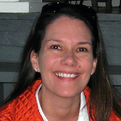 Photo of a woman with long dark hair wearing an orange jacket and smiling