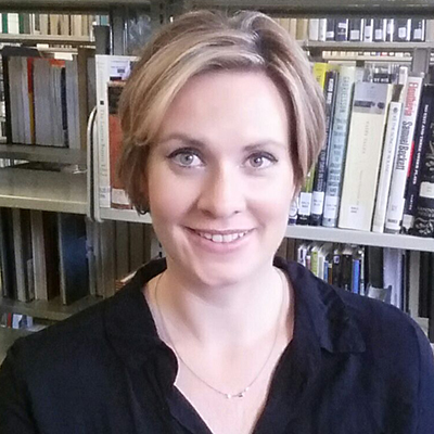 Photo of woman with short blonde hair and a black shirt smiling in front of library shelves