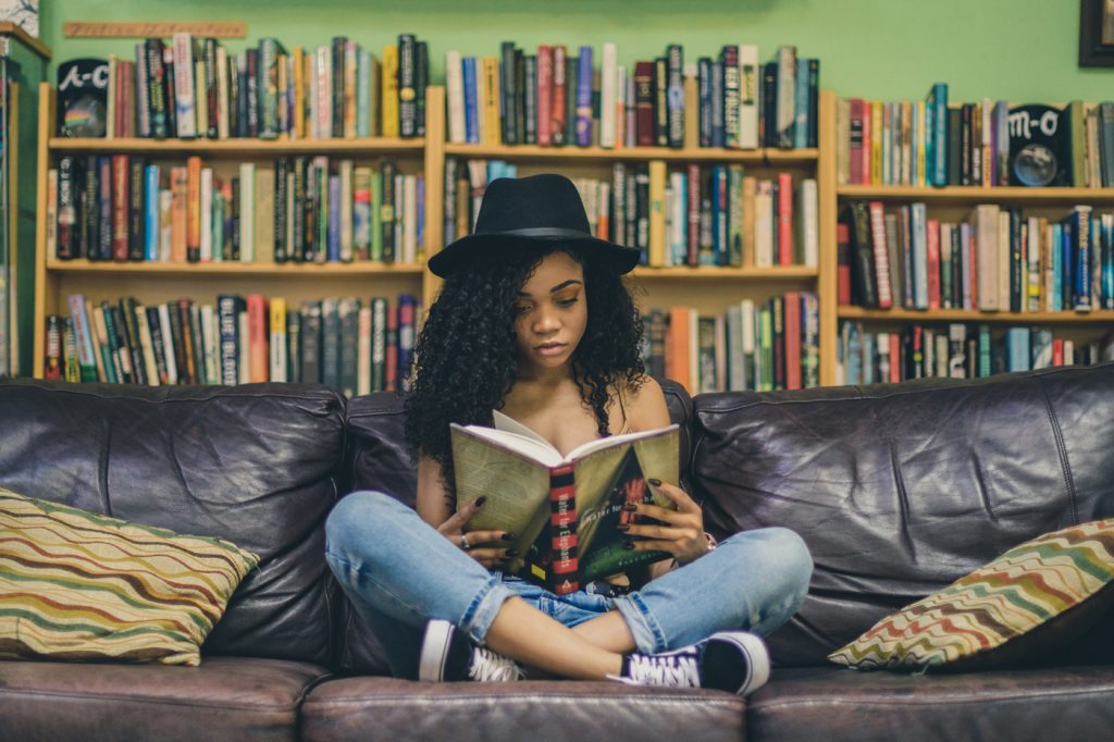 Black female teen sitting cross-legged on a couch reading in a library