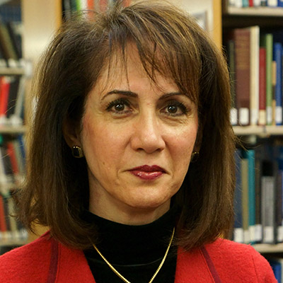 Photo of woman with dark hair and a red jacket in front of library shelves