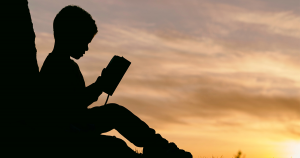 Silhouette of boy reading a book at sunset