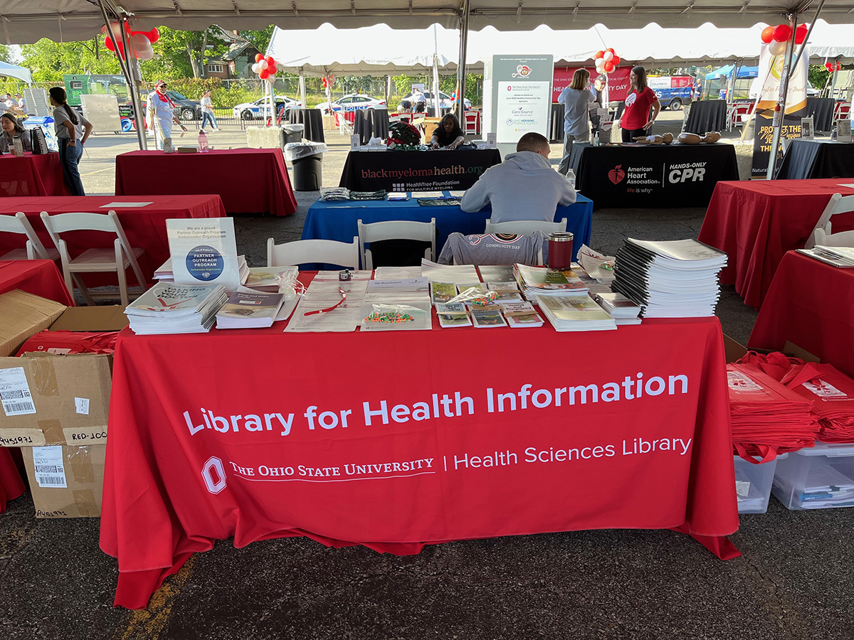 A table for The Ohio State University's Library for Health Information at a community health fair with stack of brochures and handouts.