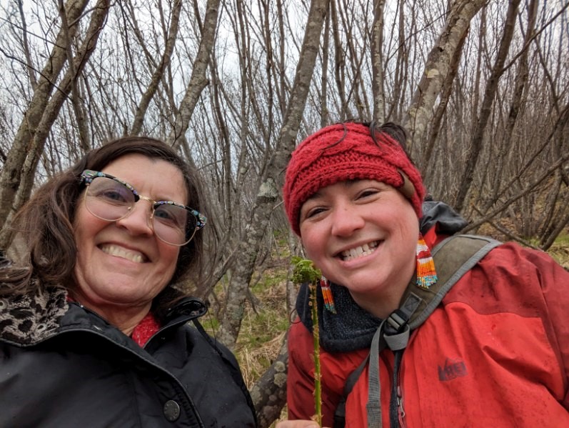 Two women in the woods holding a fiddlehead fern.