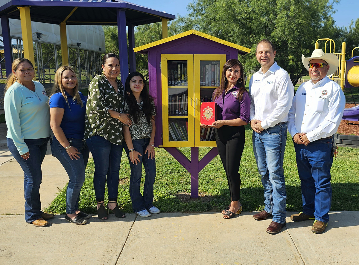 A group of people standing in front of a colorful mini library in the park