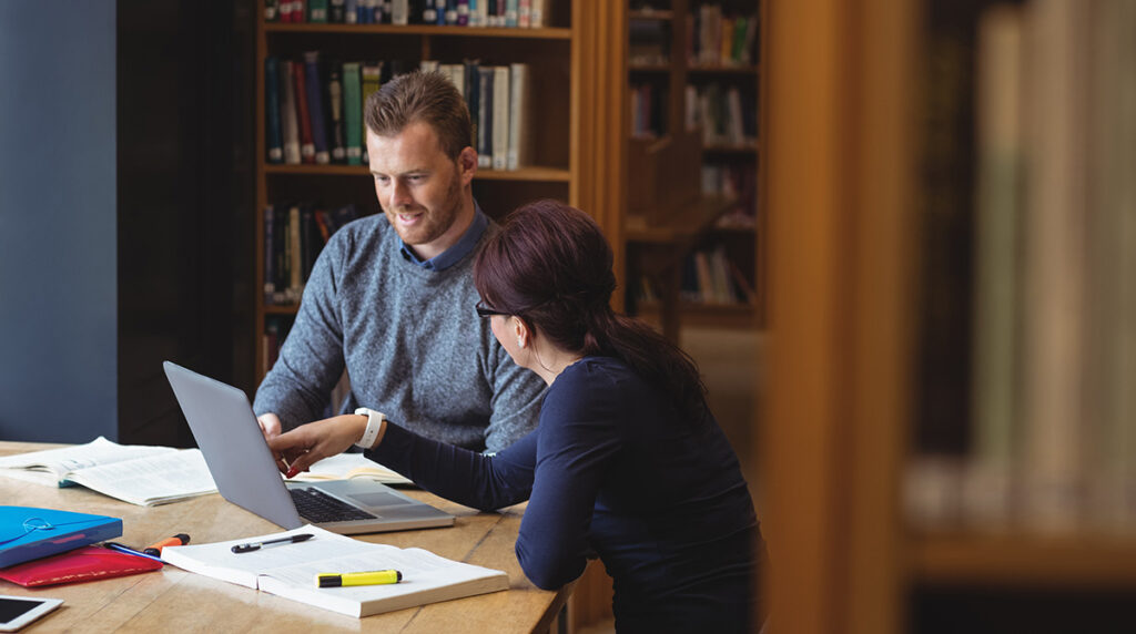 A man and woman collaborating at a table in a library