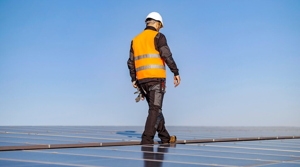 Man in an orange work vest walking on solar panels