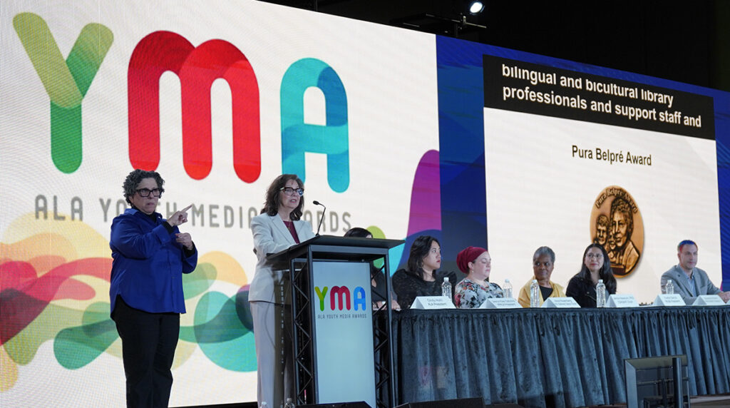 A woman behind a podium on stage presenting the Pura Belpré Award during the Youth Media Awards