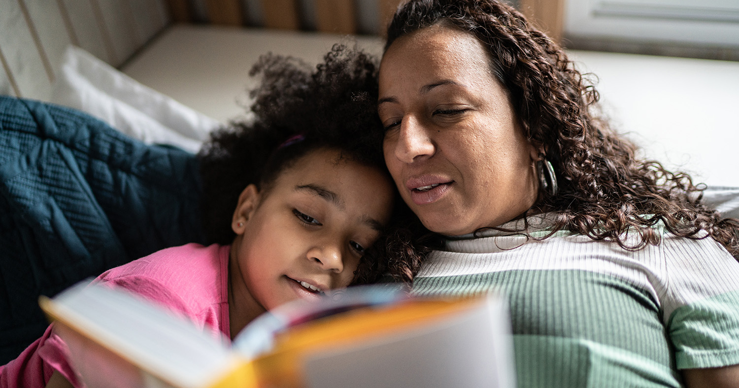 Hispanic mother laying in bed reading to daughter