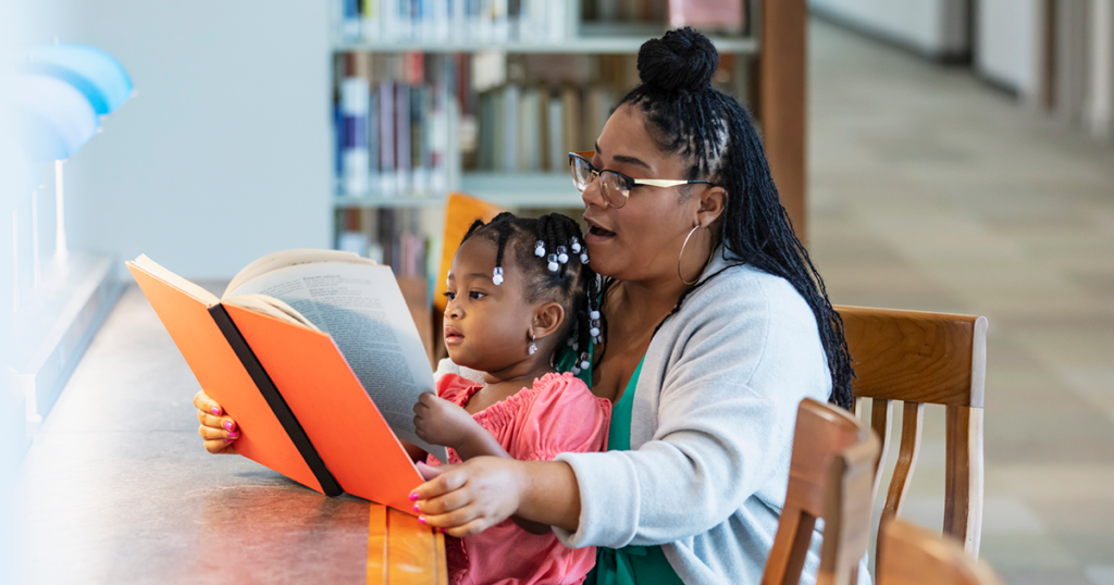 Black mother reading to young child on her lap.