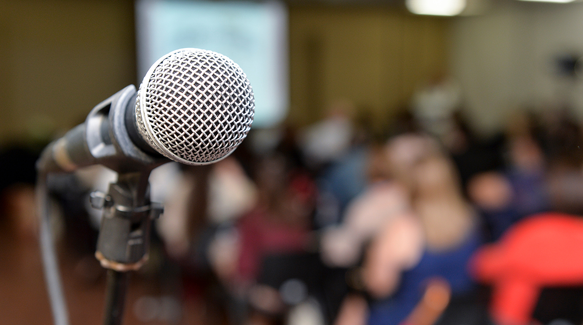 Closeup of a microphone in a room full of people.