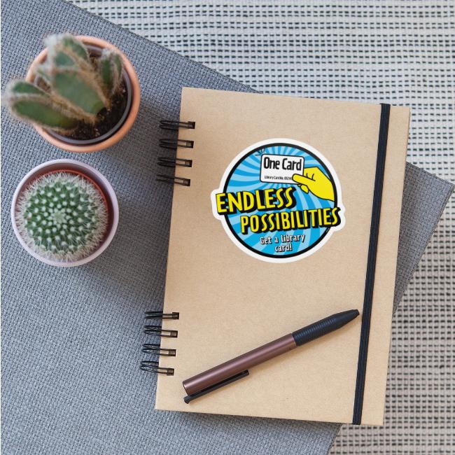Journal with a sticker with graphic that reads "One Card, ENDLESS POSSIBILITIES. Get a Library card!"