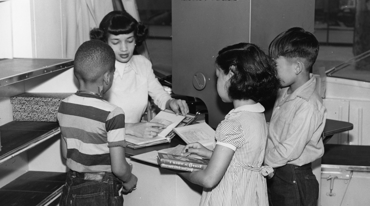 Original caption: "LOS ANGELES, October, 1949 – Elementary school pupils William Bias, Elizabeth Coggins and Jerry Sekido think it’s pretty interesting to watch Nellie Greene charge out their library books with the new Recordak charger on the Children’s Traveling Branch, operated by the Los Angeles Public Library.”