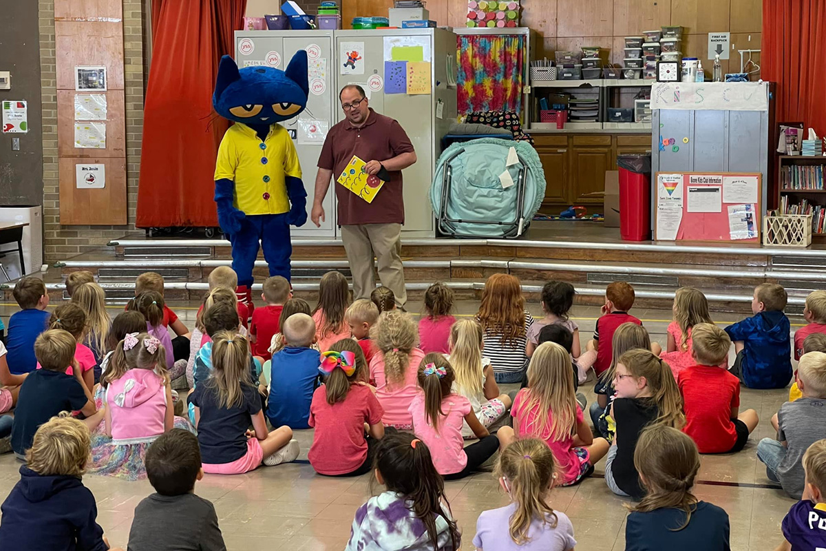 Librarian Zachary Stier standing with Pete the Cat in front of a large group of sitting children
