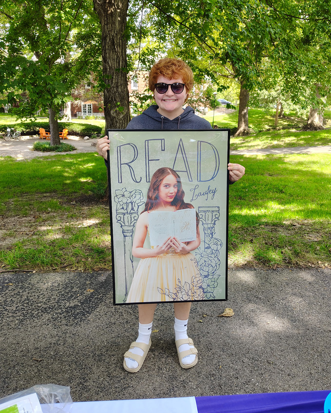 Photo of someone holding up a Laufey READ poster in a park.