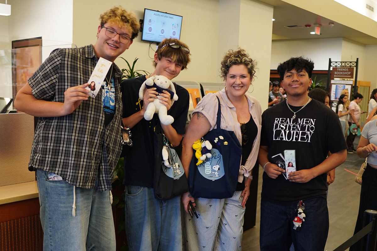 Photo of four people in a library checkout line posing with various Laufey swag.