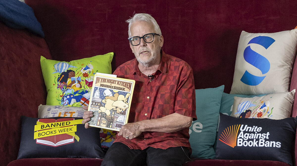 Author Andrew Larsen holds up a copy of Maurice Sendak's "In the Night Kitchen" at the Big Chair during the 2026 ALA Annual Conference.